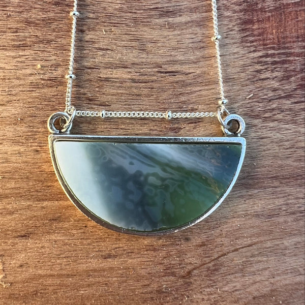 Silver necklace with a semi-circular pendant on a wooden surface